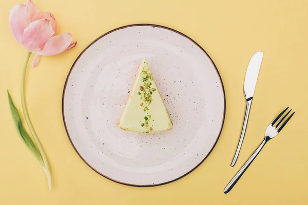 在黄色的盘子 郁金香花和餐具上的一块蛋糕的顶部视图 — 图库照片