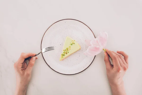 女性手 花和一块蛋糕在白色桌面上的盘子上的裁剪拍摄 — 图库照片