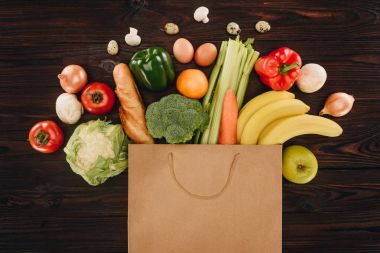 top view of different vegetables and fruits in paper bag on wooden table, grocery concept