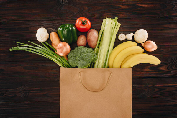 top view of different vegetables and fruits in shopping bag on wooden table, grocery concept