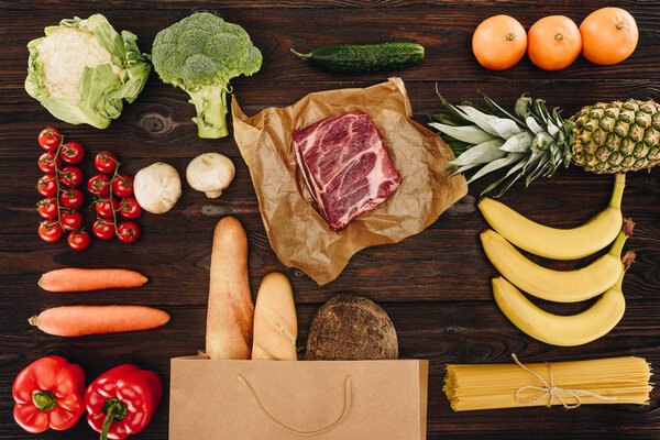 top view of raw meat with vegetables, fruits and bread on wooden table, grocery concept 