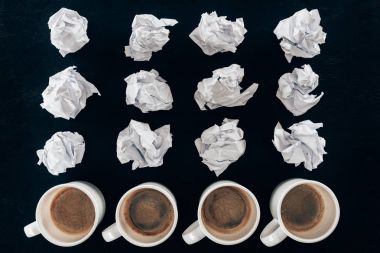 top view of crumpled papers and cups of coffee in rows isolated on black clipart