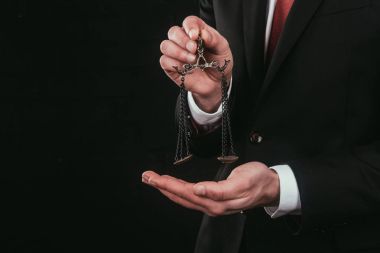 cropped shot of lawyer holding mini scales isolated on black clipart