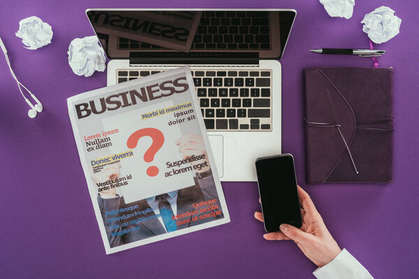 cropped shot of businesswoman using smartphone at workplace on purple surface