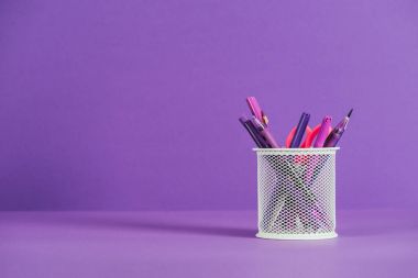 pen holder with various pens and pencils on purple surface clipart