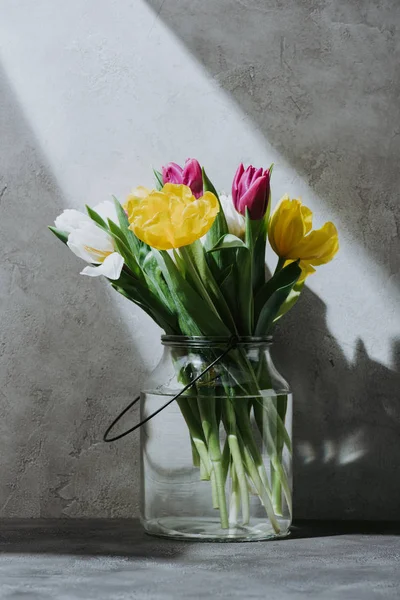 在玻璃罐子的春天郁金香花在混凝土表面与阴影 — 图库照片