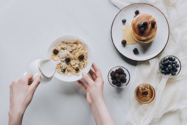 top view of person pouring milk in bowl with muesli during breakfast clipart