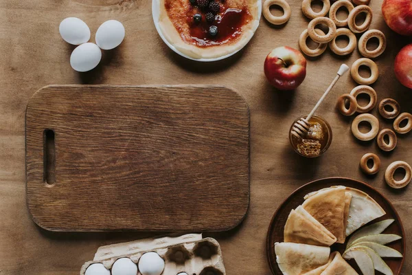 テーブルのおいしい自家製のパンケーキ 卵の箱 木製のまな板 リンゴ ベーグルのトップ ビュー  — 無料ストックフォト