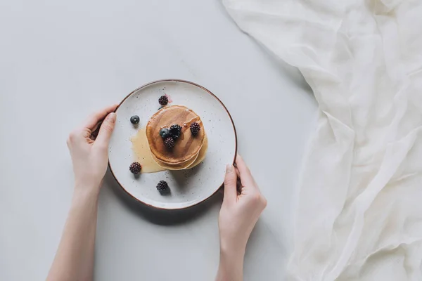 グレーに甘いおいしいパンケーキと新鮮な果実のプレートを保持している人のクロップ撮影 — ストック写真