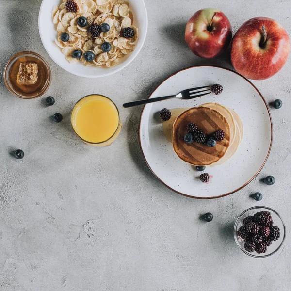 top view of sweet gourmet breakfast with pancakes, fruits, honey and muesli on grey   