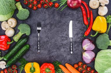 top view of fresh organic assorted vegetables and fork with knife on black clipart