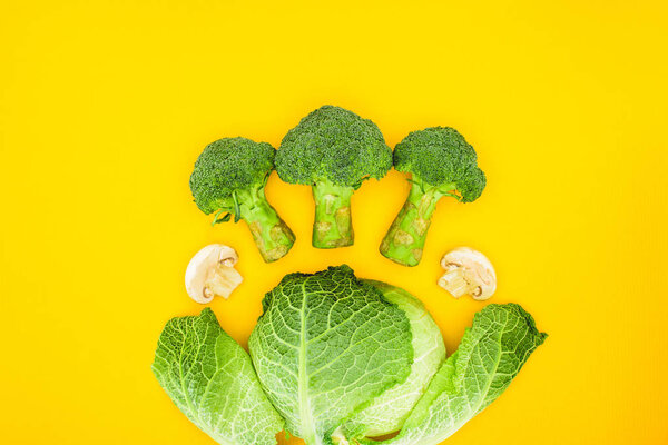 top view of fresh healthy broccoli, savoy cabbage and mushrooms isolated on yellow