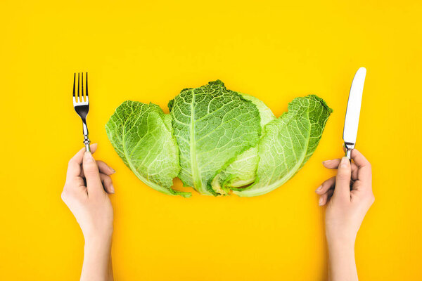 top view of person holding fork and knife while eating healthy cabbage isolated on yellow