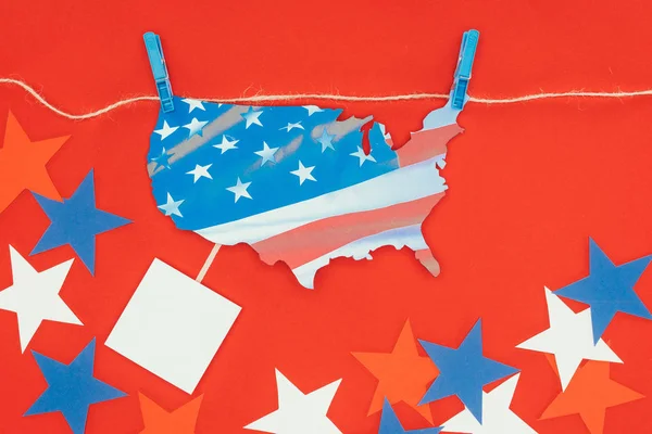 top view of piece of map with american flag hanging on rope and stars isolated on red