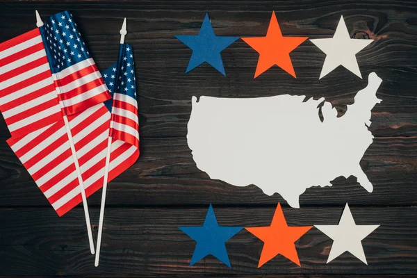 top view of arranged american flags, piece of map made of paper and stars on wooden surface, presidents day celebration concept