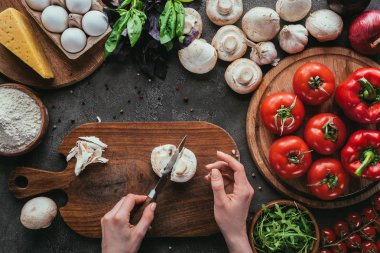 cropped shot of woman cutting mushrooms for pizza on concrete table clipart