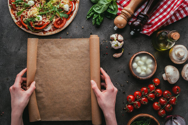 cropped shot of woman with parchent paper preparing homemade pizza on concrete table