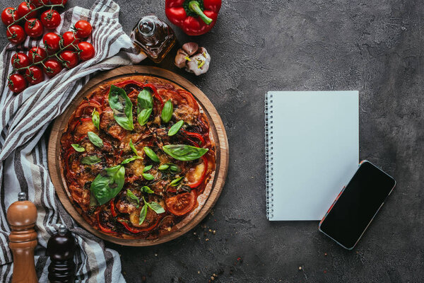 top view of freshly baked pizza with notebook and smartphone on concrete table