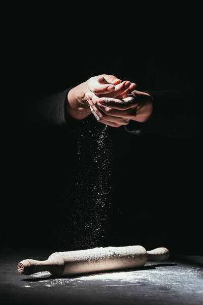 cropped shot of chef with hands covered in flour and rolling pin on table