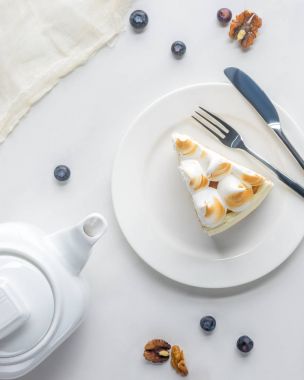 top view of appetizing piece of cake with meringue and teapot on white table clipart