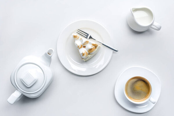 top view of appetizing piece of cake with meringue, teapot and coffee on white surface