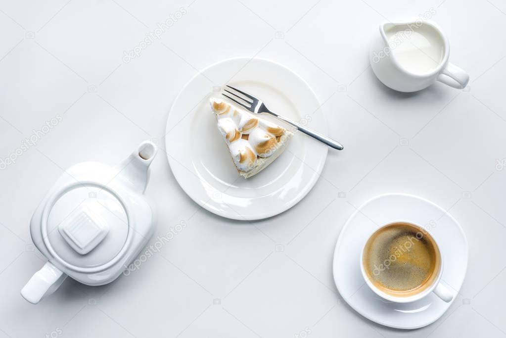 top view of appetizing piece of cake with meringue, teapot and coffee on white surface