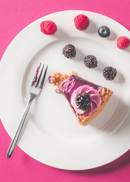 top view of bitten piece of pie with berries on plate on pink surface