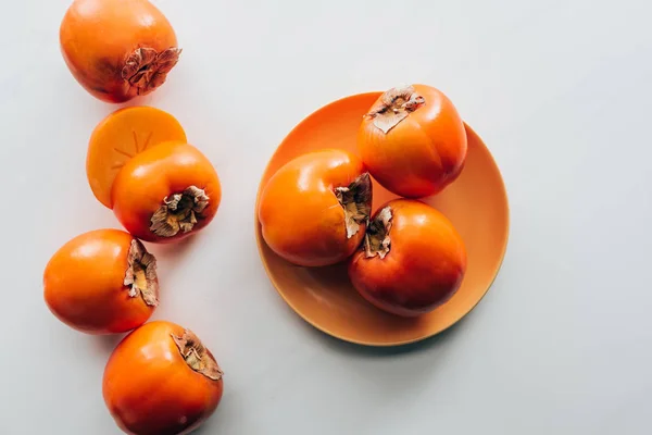 橙色盘子上的柿子和白色桌面上的顶部视图 — 图库照片