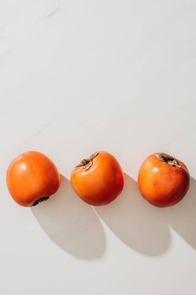 top view of three ripe persimmons on white