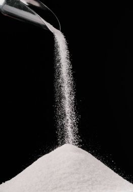 sugar falling from metal scoop on pile isolated on black
