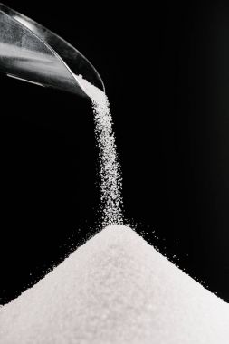white sugar falling from metal scoop on pile isolated on black clipart