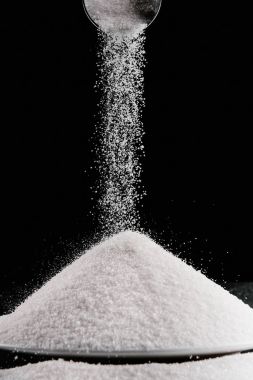 sugar falling from metal scoop on pile on plate isolated on black