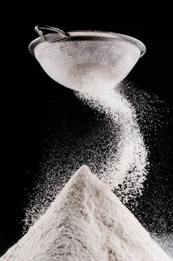 white flour falling from sieve on pile isolated on black clipart