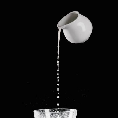 milk pouring from milk jar into bowl with flour isolated on black clipart