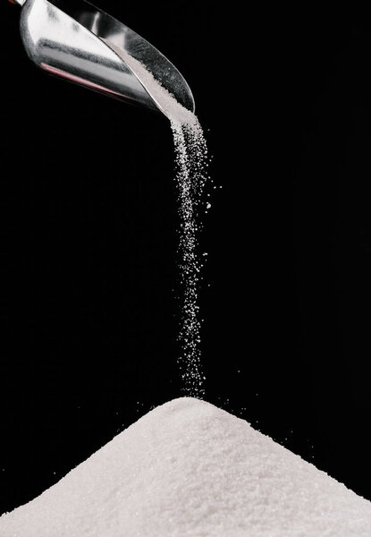 sugar falling from metal scoop on pile isolated on black