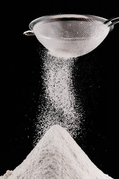 flour falling from sieve on pile isolated on black