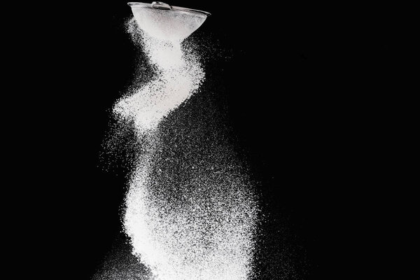 sieve with falling flour isolated on black