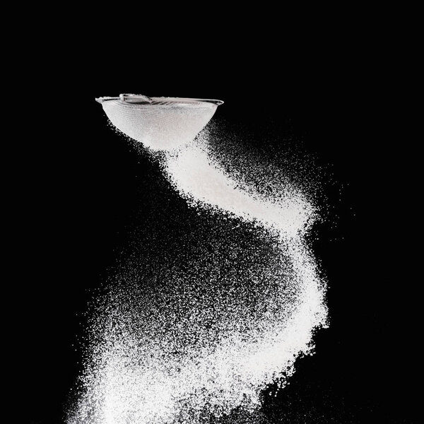sieve with falling flour isolated on black