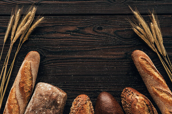 top view of arranged loafs of bread and wheat on wooden surface