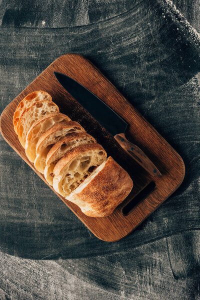 Top view of arranged pieces of ciabatta on cutting board with knife on dark surface with flour