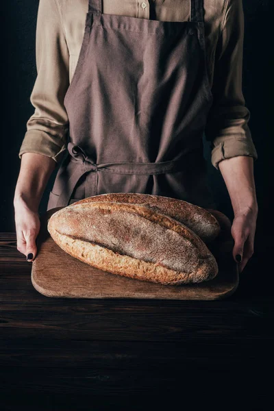 Częściowy Widok Kobietę Loafs Chleba Drewnianą Deską Krojenia Czarnym Tle — Zdjęcie stockowe
