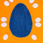 Blick von oben auf blaues Osterei aus Sand und Hühnereiern isoliert auf Orange