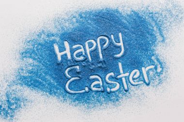 top view of happy easter sign made of blue sand on white surface clipart