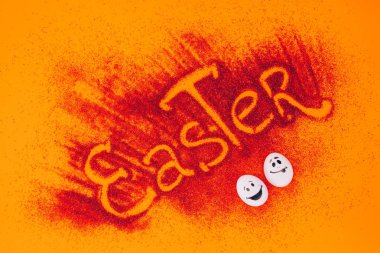 top view of easter sign made of red sand with chicken eggs with smileys on orange clipart