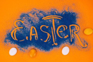 top view of easter sign made of blue sand with chicken eggs on orange clipart