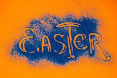 top view of easter sign made of blue sand on orange surface clipart