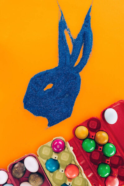 top view of bunny made of blue sand and painted easter eggs isolated on orange