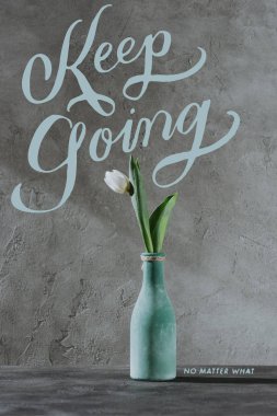white spring tulip in blue vase and KEEP GOING lettering on grey surface clipart