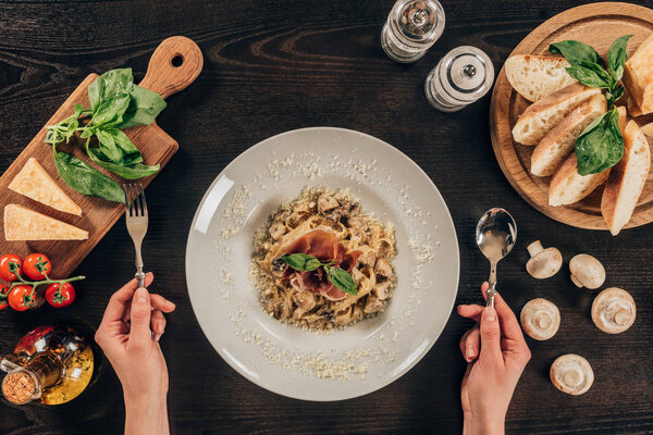 cropped image of woman holding fork and spoon and going to eat pasta
