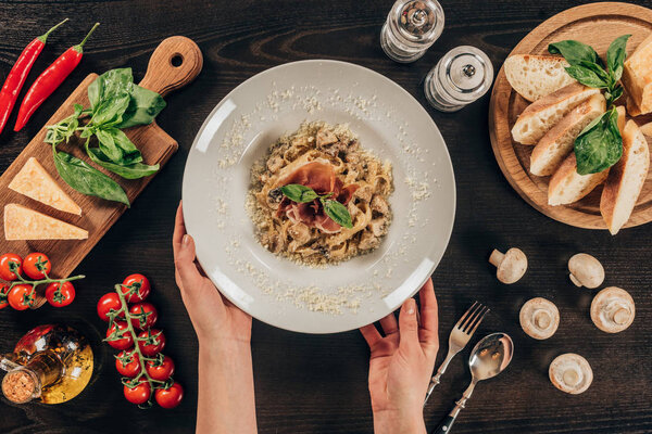 cropped image of woman putting plate with pasta on table